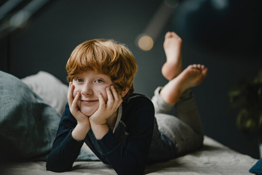 Portrait of smiling redheaded boy lying on couch at home