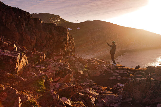 Young man taking selfie while standing on rocky mountain during sunset at Teriberka, Murmansk Oblast, Russia