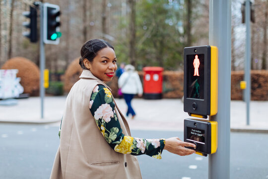 UK, London, portrait of smiling woman pressing button of pedestrian light