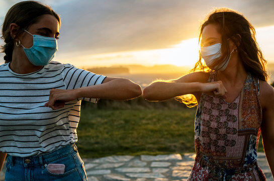 Young women in protective face masks elbow bumping against sky during COVID-19