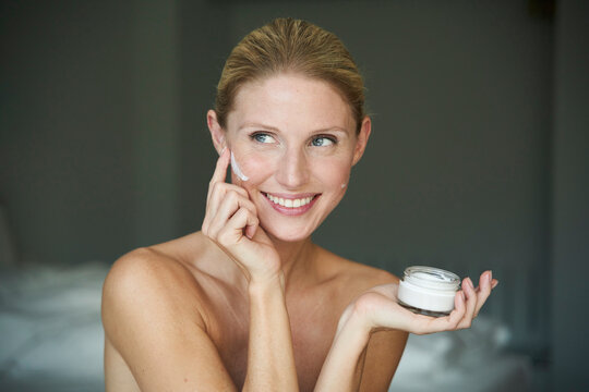 Portrait of smiling beautiful woman applying cream on her cheek