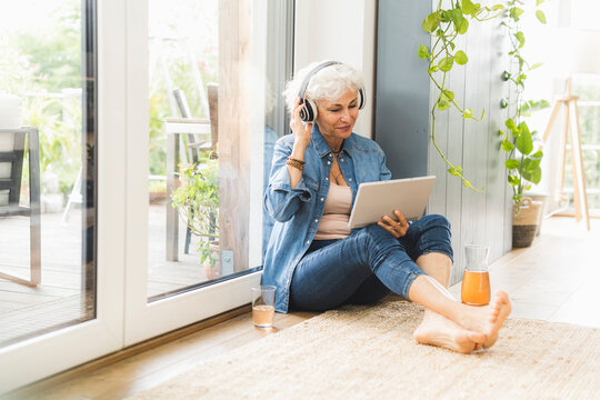 Mature woman listening to music while working on digital tablet