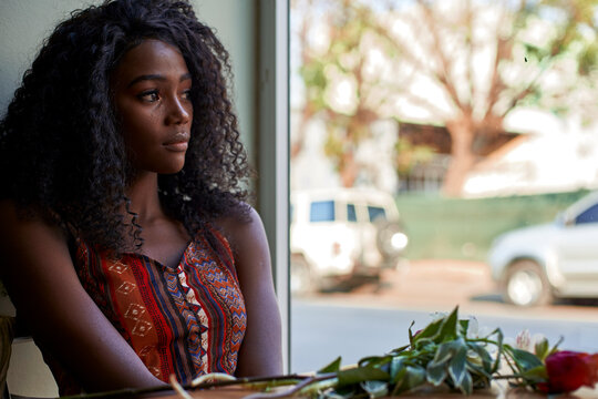 Portrait of young African woman with flowers on the table in a cafe, looking out of window