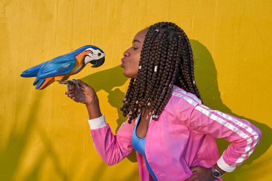 Woman kissing a wooden parrot on a yellow wall