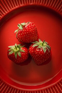 Three fresh strawberries on a red plate