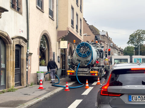 Strasbourg, France - Sep 9, 2025: Heating oil tanker truck with blue hoses delivering fuel on urban street in Strasbourg with traffic cones, pedestrian, Volvo car and historic architecture.