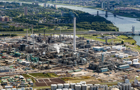 Aerial view of a large oil refinery complex at a coastal port, featuring industrial storage tanks and pipelines.