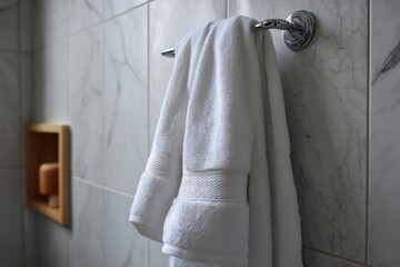 Close up of soft white towel hanging on metal holder against gray textured bathroom wall, showcasing clean modern home interior.