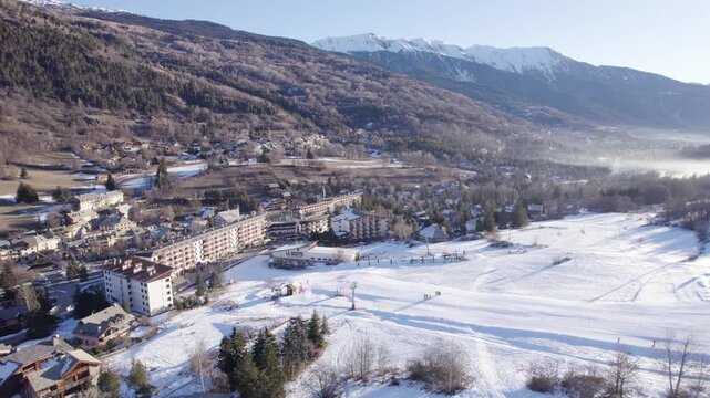 Aerial winter view of an alpine ski resort village with snowy slopes, hotels and mountains, ideal for travel, tourism, and real estate visuals.