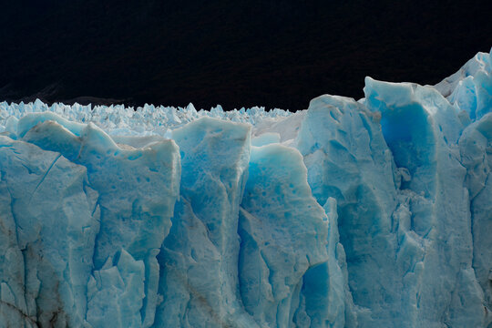View of a colossal, textured glacier face with striking blue hues against a dark sky, an icy behemoth in Los Glaciares National Park, Santa Cruz Province, Argentina.