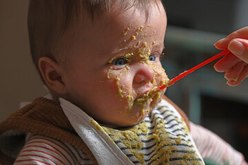 baby eating with a spoon and playing with food, with marks on its face