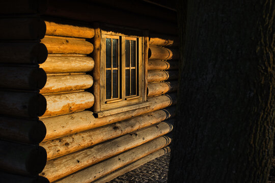 Detail of a traditional log cabin with window in golden hour sunlight, rustic wooden wall