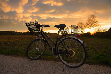 silhouette of city bike with two baskets, beside fields. sunset scenery with mammatus clouds