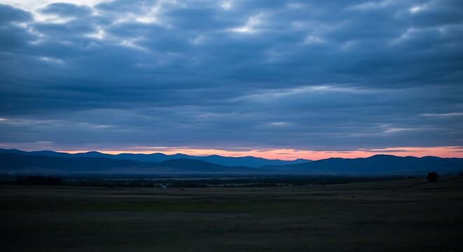 Evening vista fields & mountains silhouetted under a dramatic, layered, cloudy sky