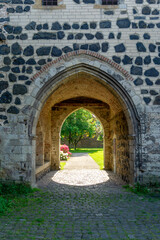 Obraz premium Historic Gothic Stone Archway and Medieval Masonry in Zons Germany overlooking a Sunlit Summer Garden with Flowers and Cobblestone Paving