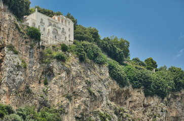 Fototapeta premium Distinctive white historic villa or castle structure perched dramatically on steep rocky cliff face with Mediterranean architectural details.