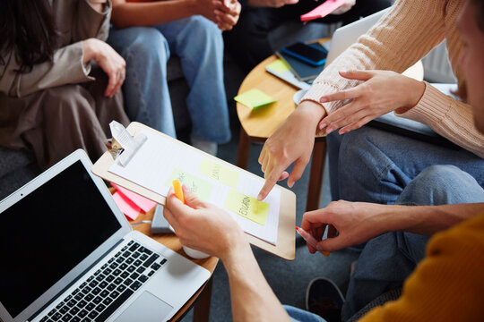 Hand of female entrepreneur pointing on adhesive note stuck on clipboard held by male colleague while discussing in office