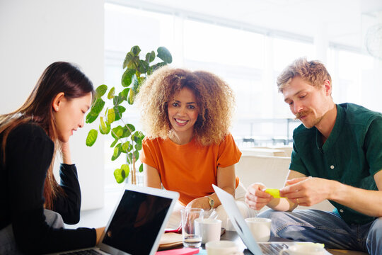 Portrait of smiling curly haired businesswoman sitting with coworkers in office lobby