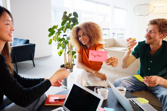 Portrait of smiling curly haired female entrepreneur showing adhesive note with together word written on it