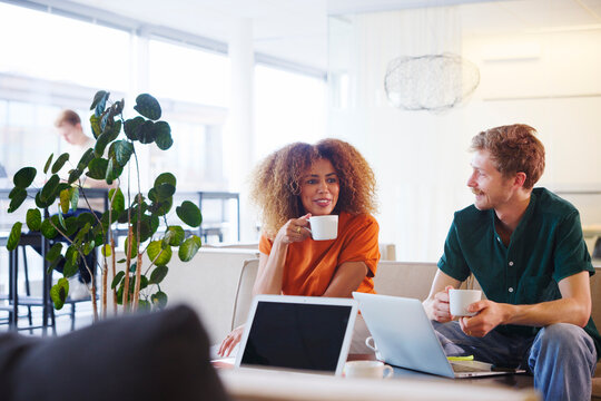 Smiling curly haired businesswoman taking coffee break with male colleague in office lobby