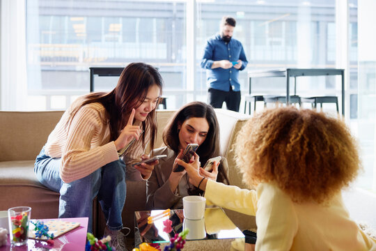 Female business experts using smart phone while spending leisure time in office lobby