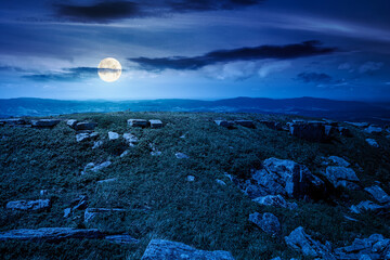 grassy alpine meadow in carpathian mountain landscape at night. sharp rocks and huge boulders among lush grass on rolling hills in full moon light. open space scenery for wanderlust and exploration © Pellinni