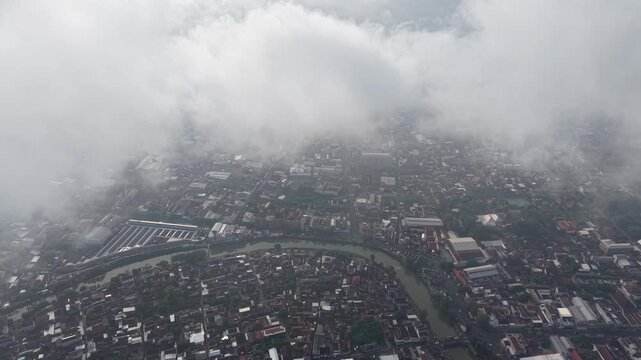 Birds-eye view of a sprawling river city with dense neighborhoods, winding waterway, and visible infrastructure as clouds drift overhead, conveying scale, motion, and atmospheric conditions.