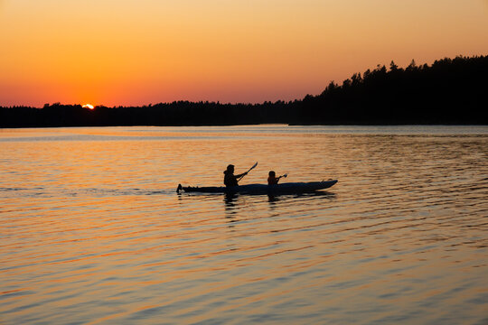 In silhouette shot of father and daughter rowing boat in sea at sunset