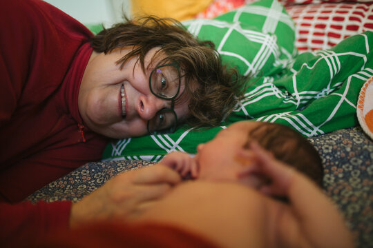 Smiling senior woman adoring her newborn grandson while lying on bed at home