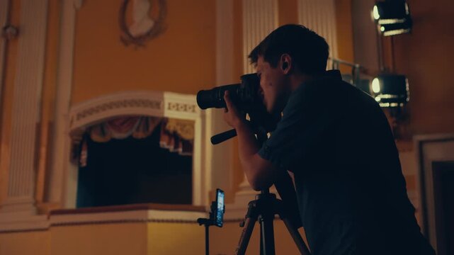 A photographer at a concert looks through the viewfinder and takes a photo. A young male photographer holds a camera taking pictures. Reportage shooting of the concert.