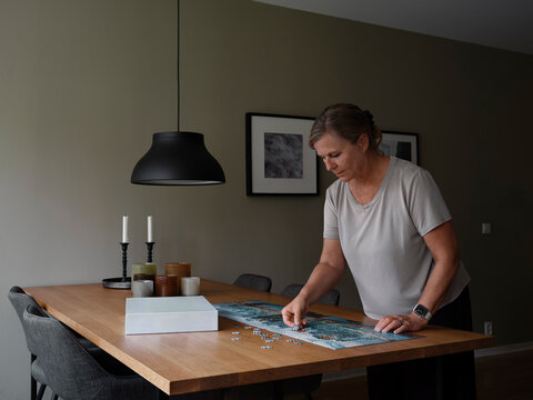 Woman solving jigsaw puzzle on table at home