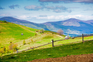 green rural landscape with wooden fence. countryside scene with rolling hill in spring. pastoral highland region on cloudy weather. environment sustainability and protection. background for earth day