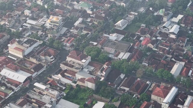 An aerial shot of a dense urban neighborhood showcasing red-tiled roofs, lush trees, and a mix of traditional and modern buildings, conveying city life and community in a compact area.