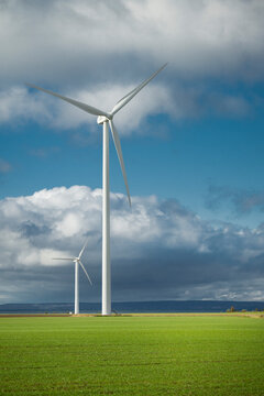 Wind turbines spinning in field against cloudy sky