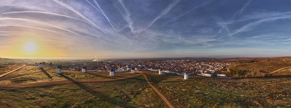 Aerial view of windmills standing tall against the rising sun, casting long shadows across the grassy hills, Campo de Criptana, Castile-La Mancha, Spain.