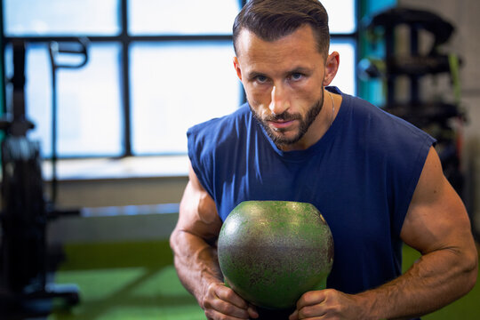 Portrait of man with muscular build holding kettle bell in gym