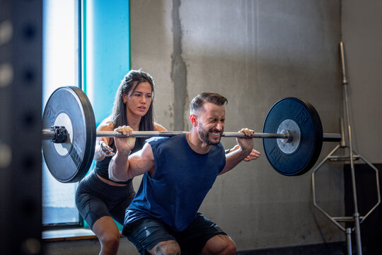 Dedicated male athlete doing squats with female friend in gym