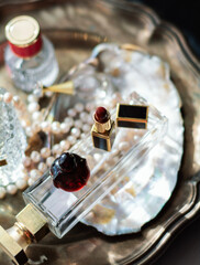 Luxury beauty flat lay: deep red perfume, gold lipstick, black case on iridescent mother-of-pearl tray with natural pearls. Soft dreamy lighting, romantic glow, feminine elegance 