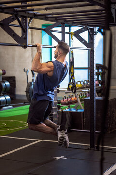 Full length of male athlete doing chin-ups on bar in gym
