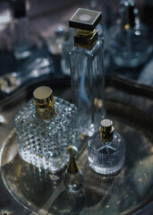 Moody luxury still life of elegant crystal and glass perfume bottles with gold accents arranged on a dark metallic tray. glamour for beauty, fragrance, and high-end lifestyle