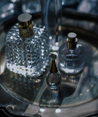 Moody luxury still life of elegant crystal and glass perfume bottles with gold accents arranged on a dark metallic tray. glamour for beauty, fragrance, and high-end lifestyle