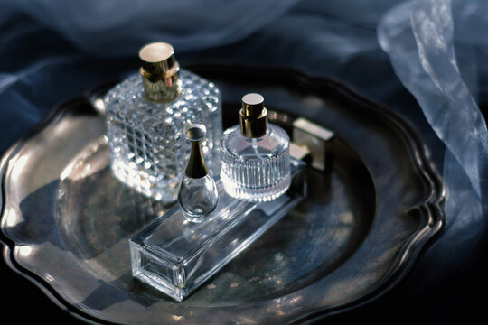 Moody luxury still life of elegant crystal and glass perfume bottles with gold accents arranged on a dark metallic tray. glamour for beauty, fragrance, and high-end lifestyle