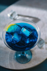Electric blue cocktail in elegant martini glass with ice cubes and fresh lime slice. Moody dramatic lighting, sophisticated top-down view &mdash; perfect for luxury bar, party and summer refreshment concept