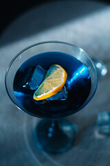 Electric blue cocktail in elegant martini glass with ice cubes and fresh lime slice. Moody dramatic lighting, sophisticated top-down view &mdash; perfect for luxury bar, party and summer refreshment concept