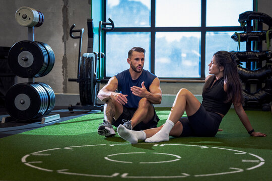 Male coach talking with woman while sitting on floor in gym