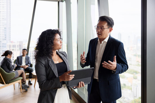 Male manager discussing strategies with female colleague holding digital tablet at office