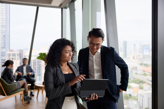 Smiling female employee showing digital tablet to manager at office