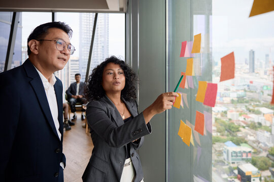 Female entrepreneur explaining ideas on adhesive notes to manager in office meeting