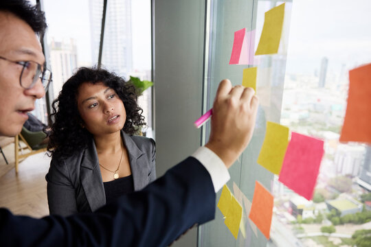 Female colleague next to manager writing on adhesive note at office