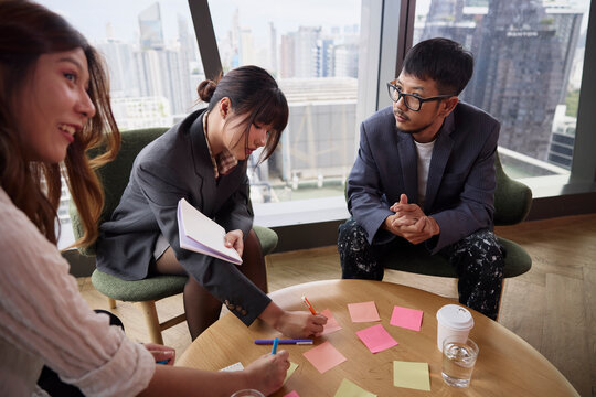 Young male and female entrepreneurs writing on adhesive notes in team meeting